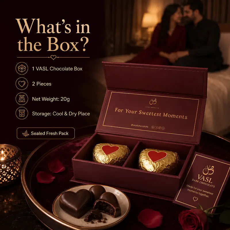 A boxed chocolate gift set displayed on a tray in a romantic bedroom scene. The open burgundy box contains two gold-wrapped chocolates with red heart labels, and a card reading 'VASI Sweet Chocolates' is shown beside it.